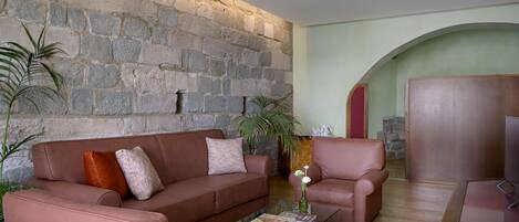 A living room with a stone wall, a brown leather sofa, a glass coffee table, and a wooden cabinet.