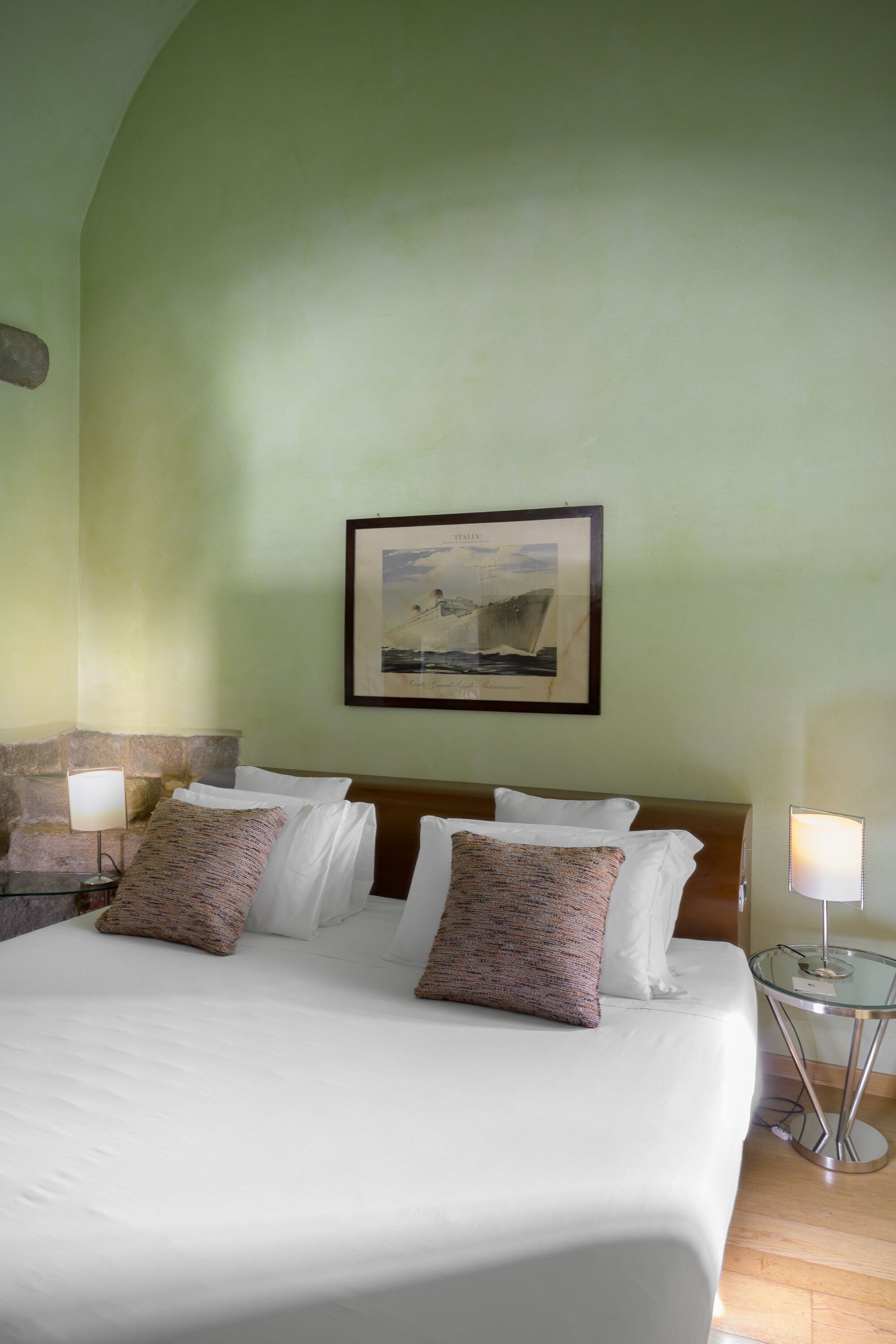 A hotel room with a bed, two bedside lamps, a framed picture on the wall, and a stone accent wall.