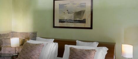 A hotel room with a bed, two bedside lamps, a framed picture on the wall, and a stone accent wall.