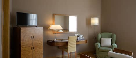 Una habitación de hotel con un armario de madera, un escritorio con lámpara, un sillón verde y una cama.