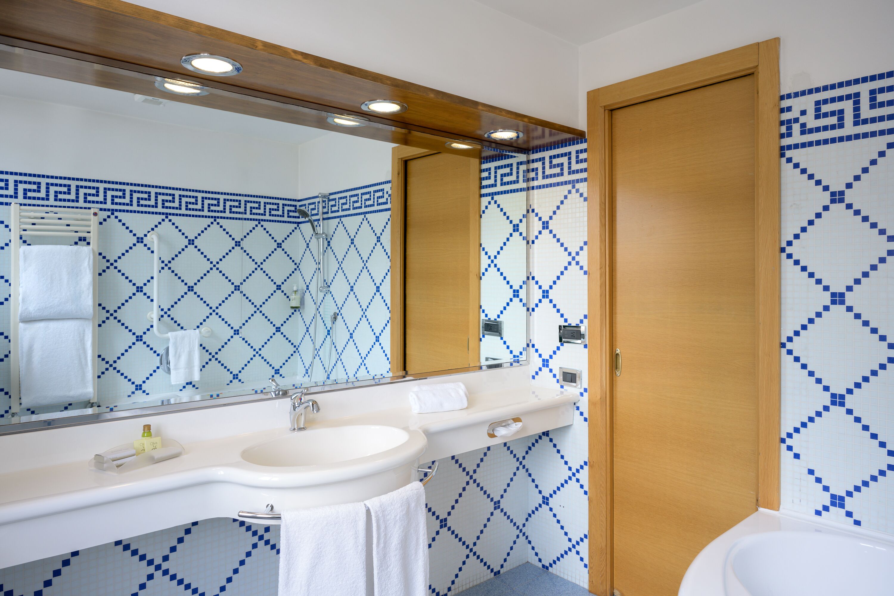 A bathroom with a white sink, a mirror, and a shower. The walls have a blue and white geometric pattern.