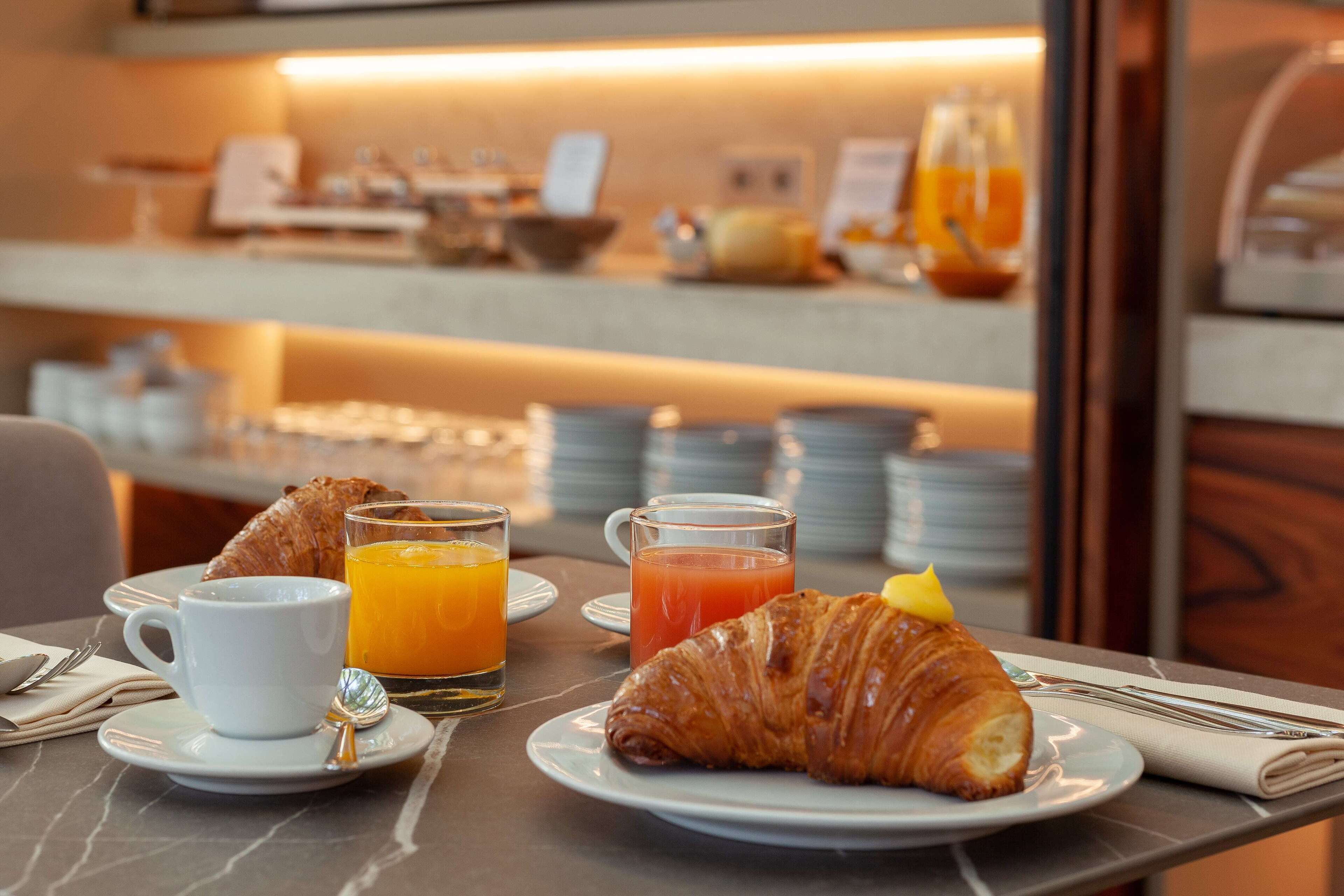 Un desayuno con cruasanes, jugo de naranja y una taza de café sobre una mesa de mármol.