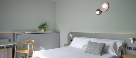 Habitació d'hotel moderna amb llit, escriptori, cadira i taula petita.