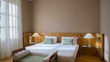 A hotel room with a large bed, two bedside tables with lamps, a wooden headboard, and a window with curtains.