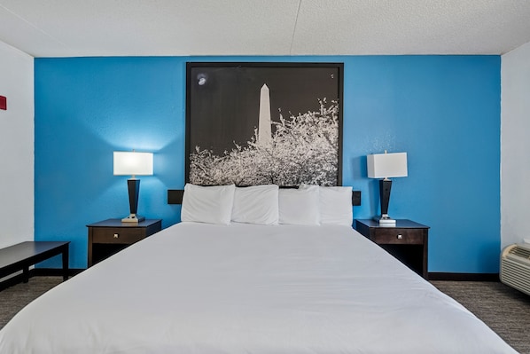 A hotel room with a large bed, two bedside tables with lamps, a nightstand, and a wall-mounted picture of a monument.
