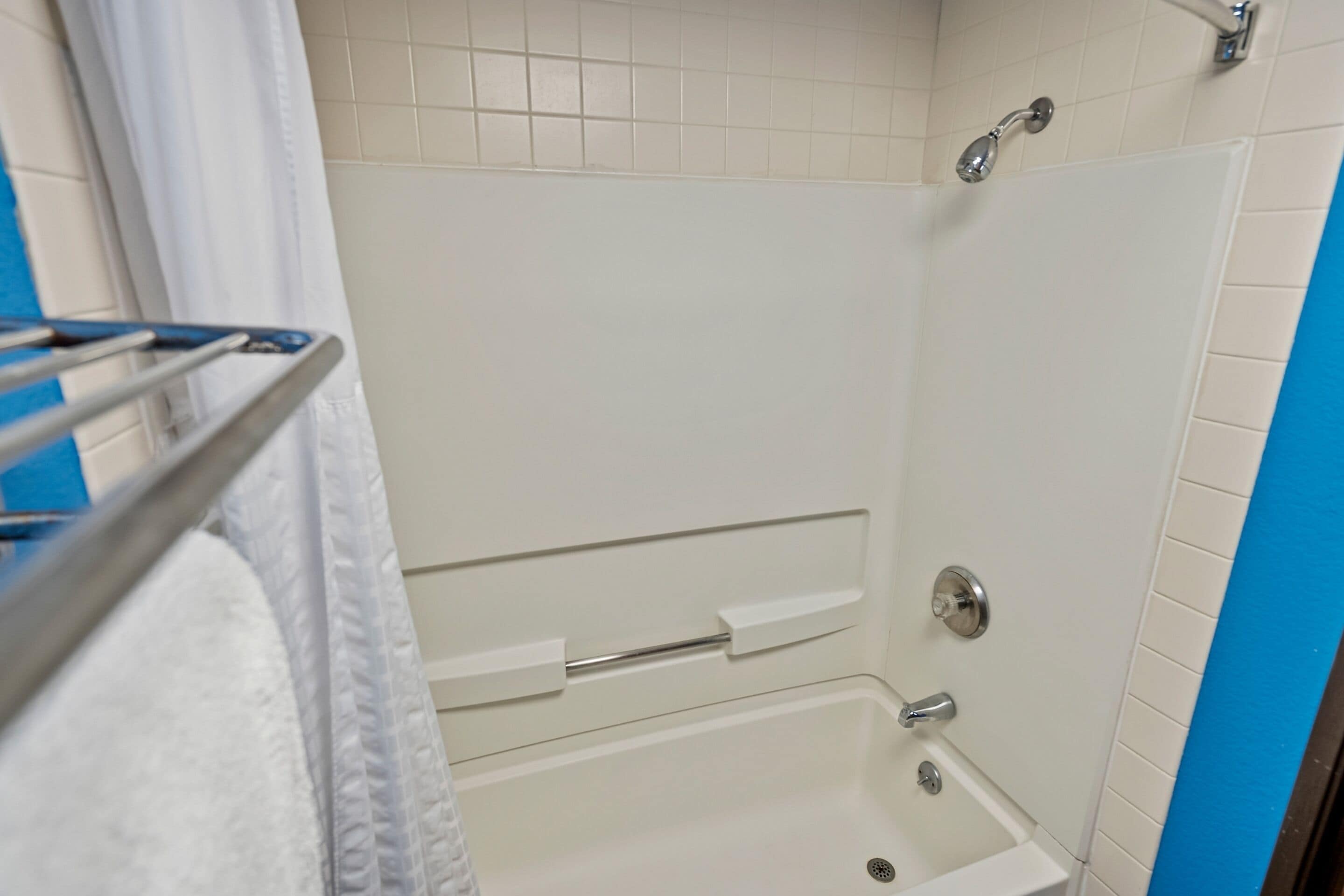 Un baño con ducha, toallero y pared con azulejos blancos.