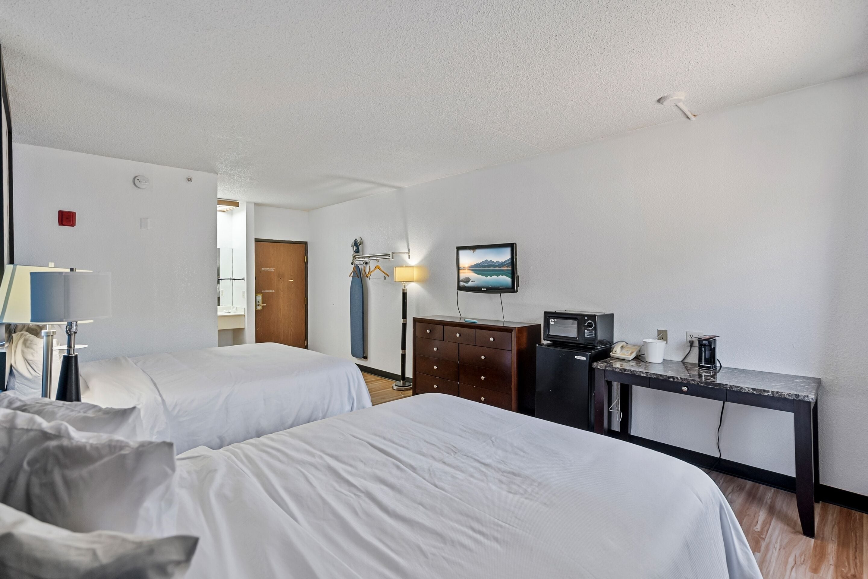 Een hotelkamer met twee bedden, een bureau met een computer, een lamp en een televisie aan de muur.