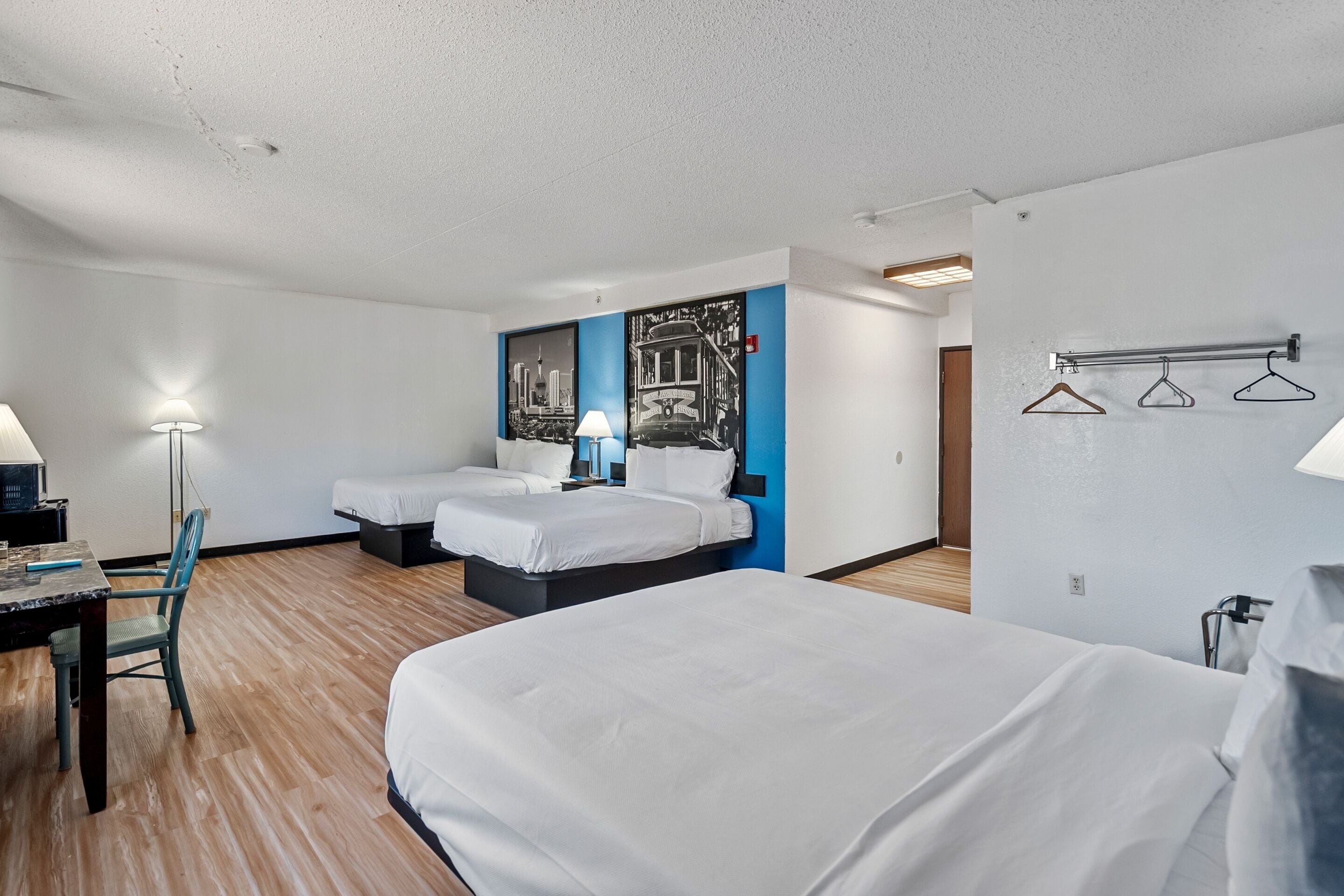 A hotel room with two beds, a desk, a chair, a lamp, and a wall-mounted coat rack.