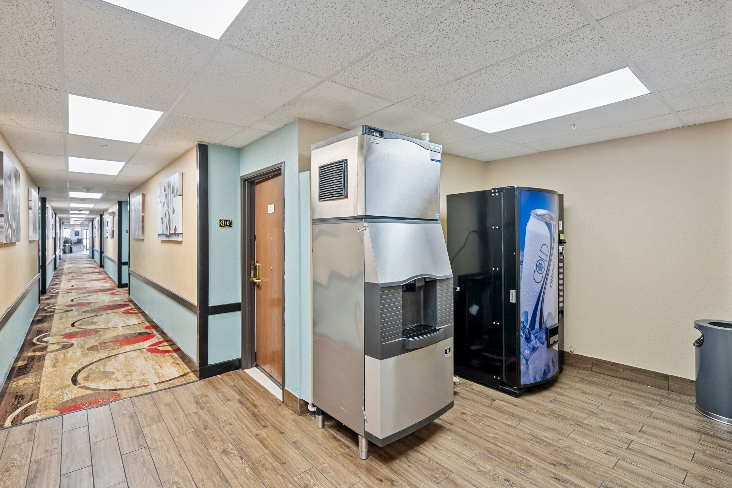 Un pasillo de hotel con un dispensador de agua, un refrigerador y una máquina expendedora.