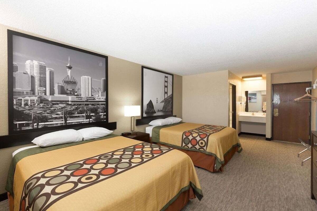 A hotel room with two beds, a cityscape poster, a mirror, and a door.