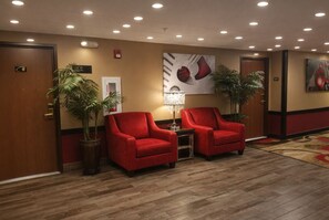 A lobby with two red armchairs, a floor lamp, and potted plants.