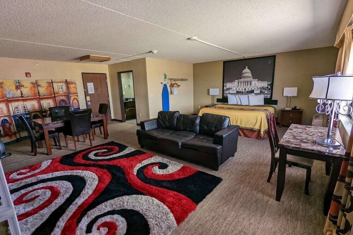 A hotel room with a bed, a sofa, a dining table, a desk, and a large rug.