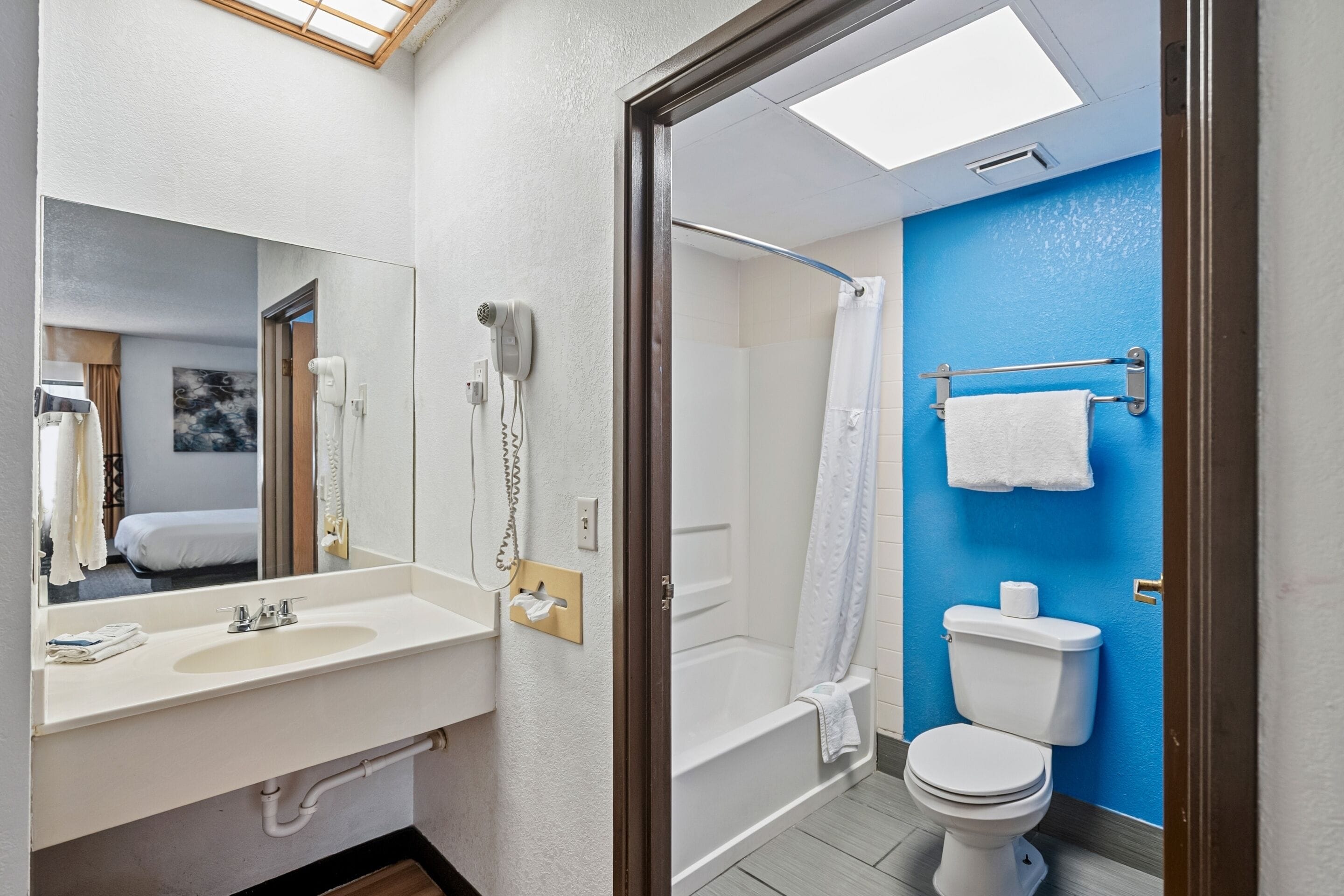 Een badkamer met een wastafel, spiegel, haardroger, douche en toilet.