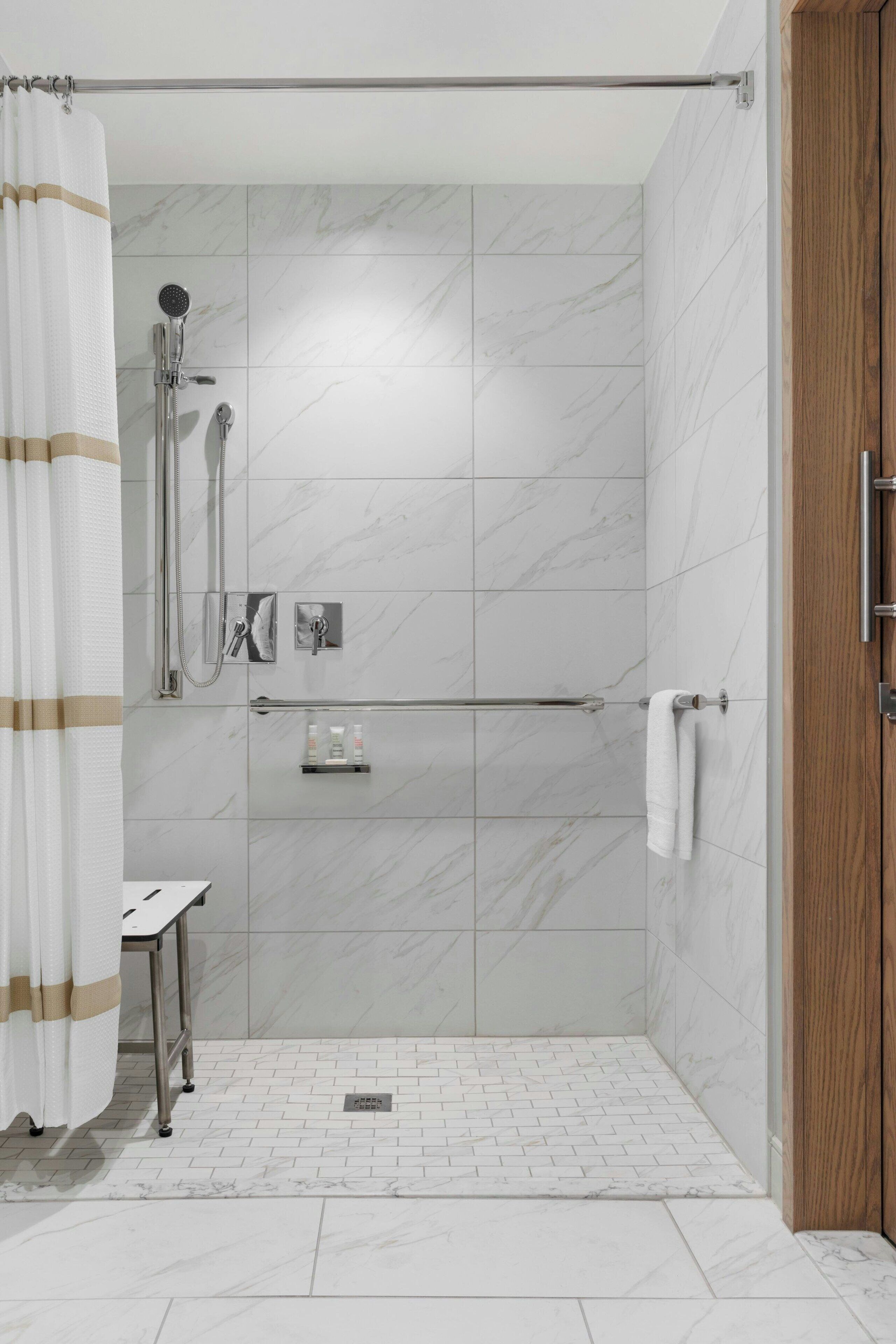 Un espace douche moderne doté d’une porte en verre, d’un pommeau de douche à main, d’un porte-serviettes et d’une petite étagère pour les articles de toilette.