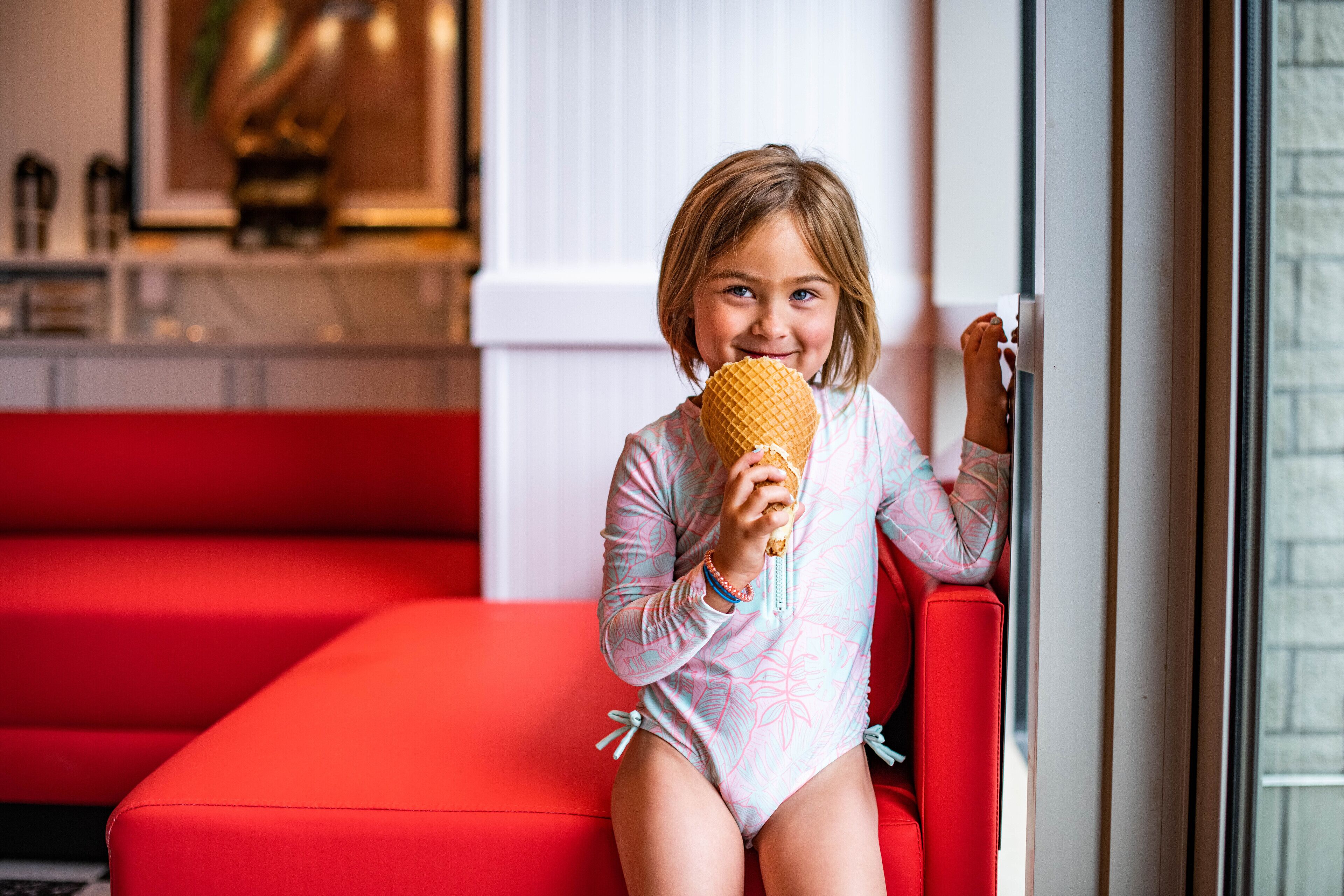 A child sitting on a red couch in a modern room with a window and a kitchen area in the background.