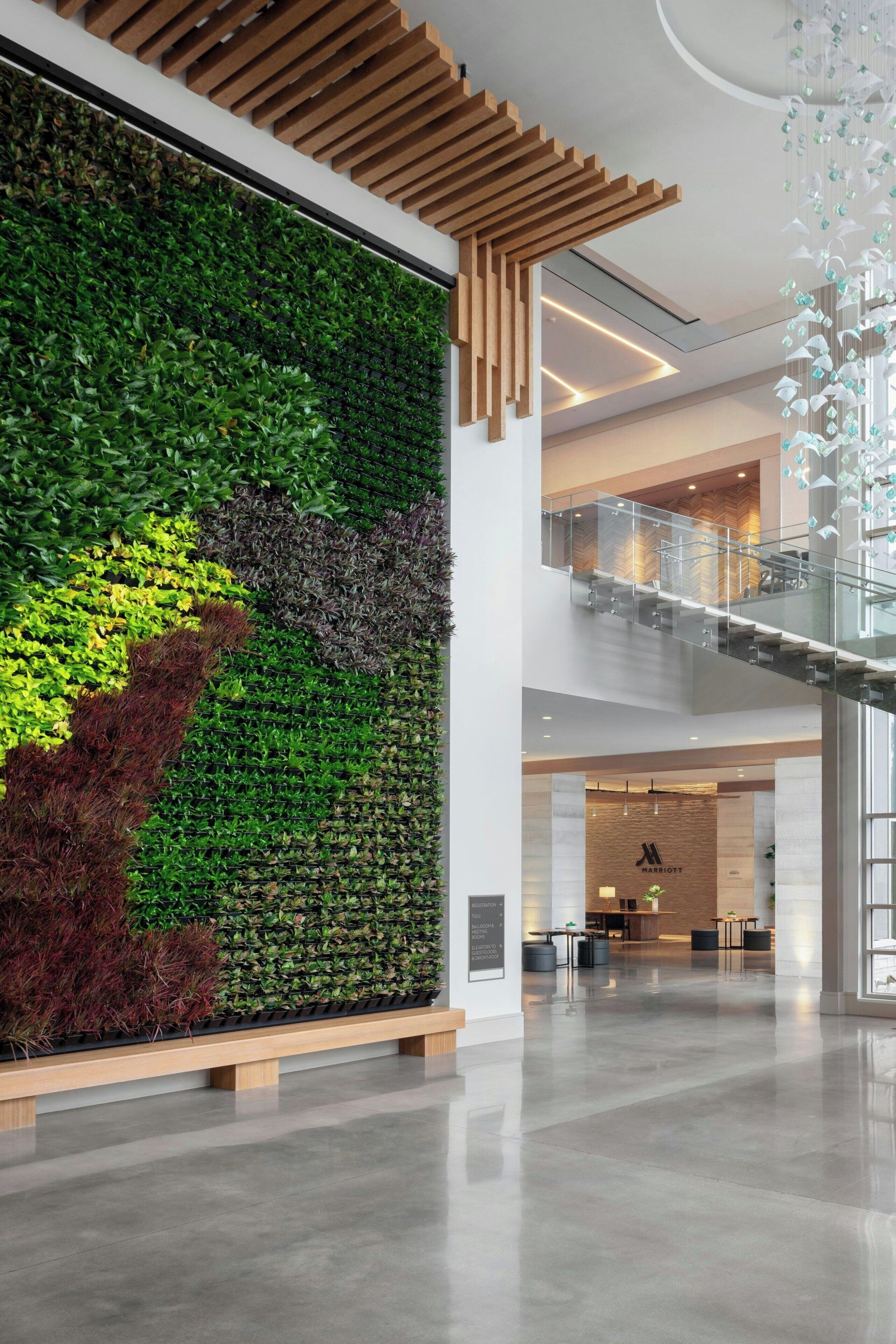 A modern hotel lobby with a large vertical garden, a mezzanine level, and a glass railing.