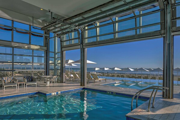 Una piscina techada, una piscina al aire libre, sombrillas