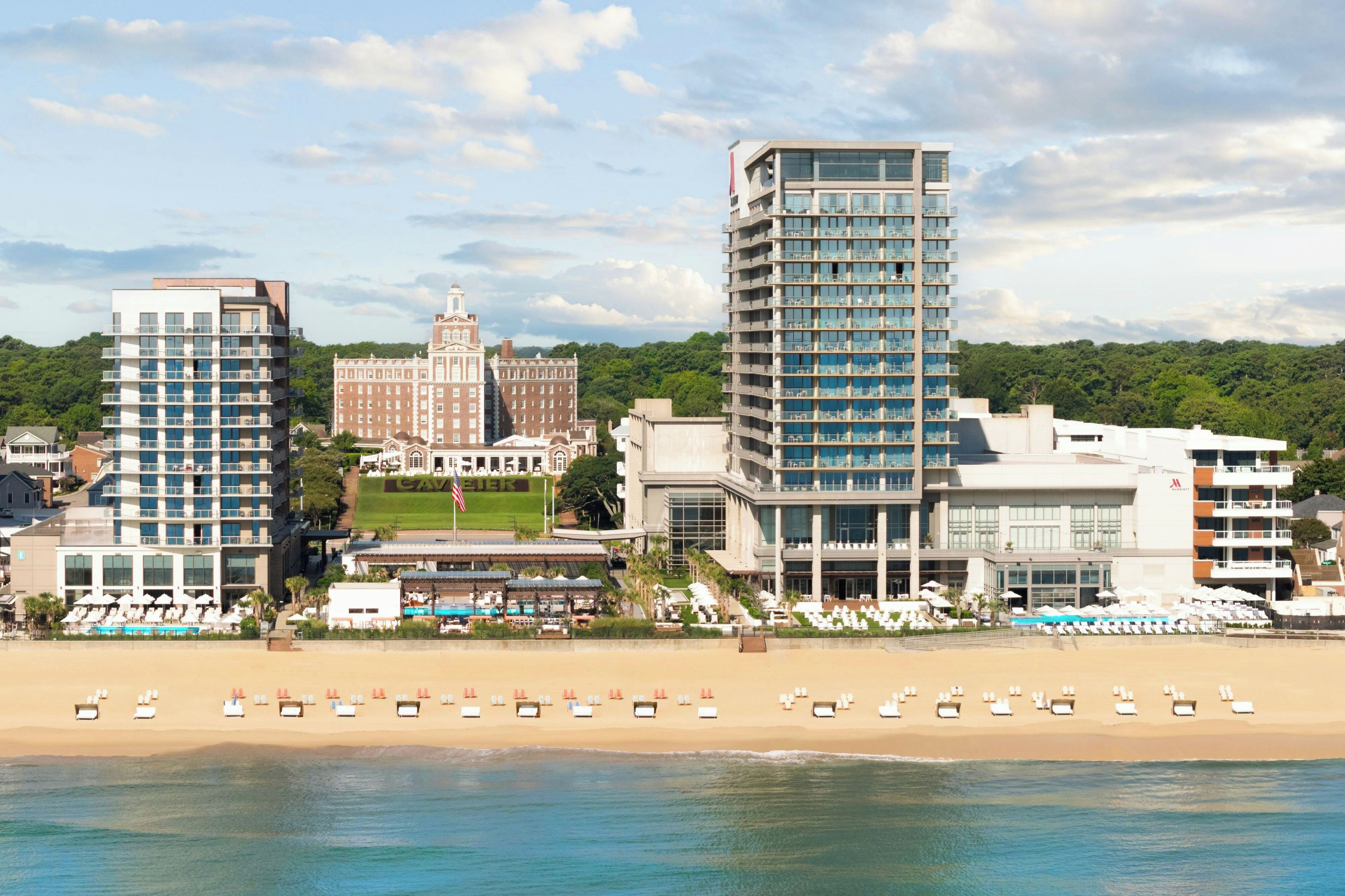 A beachfront hotel with multiple high-rise buildings, a pool area, and beach chairs.