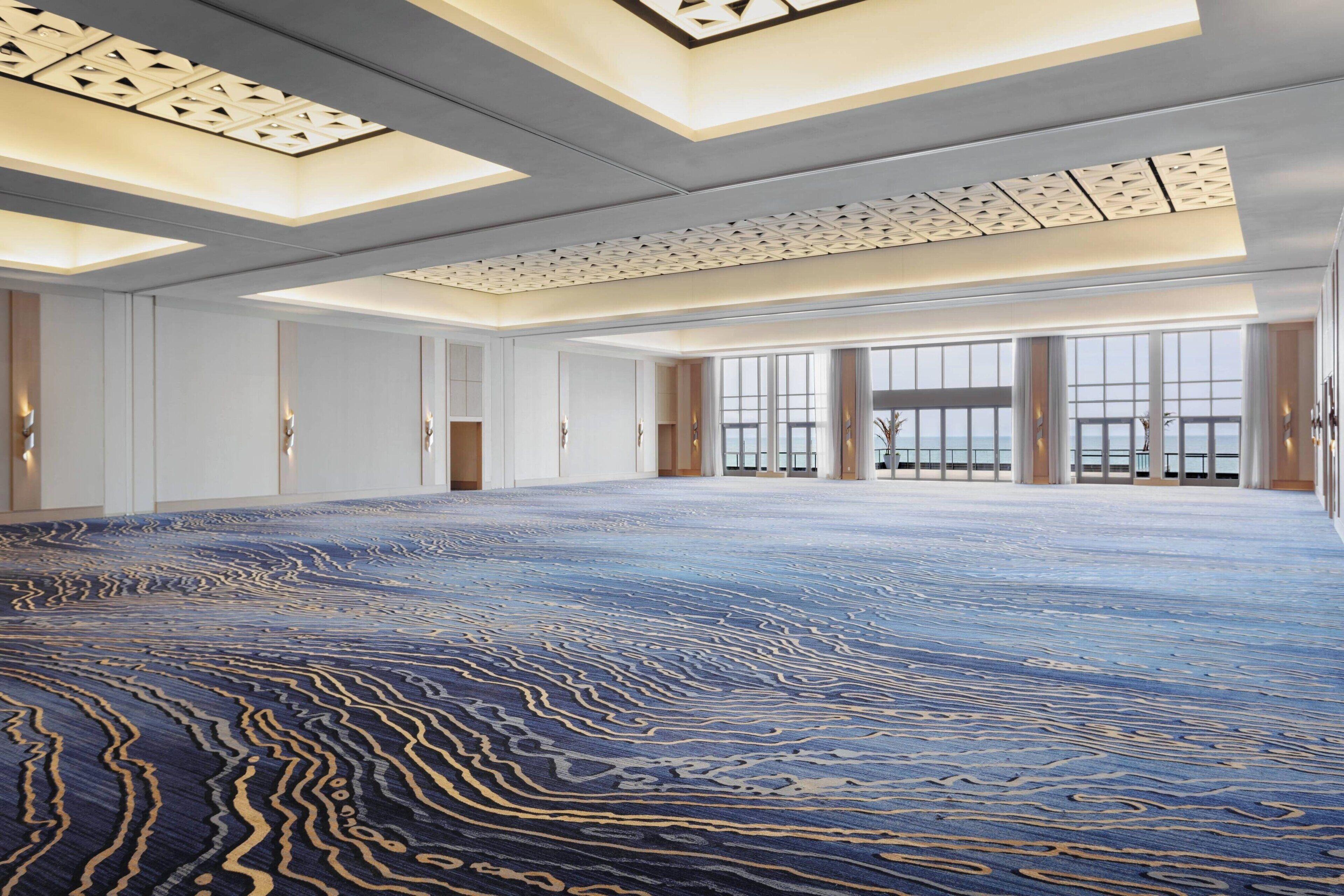 Een ruime hotellobby met een kamerbreed tapijt, grote ramen en een hoog plafond met gedetailleerde verlichtingsarmaturen.