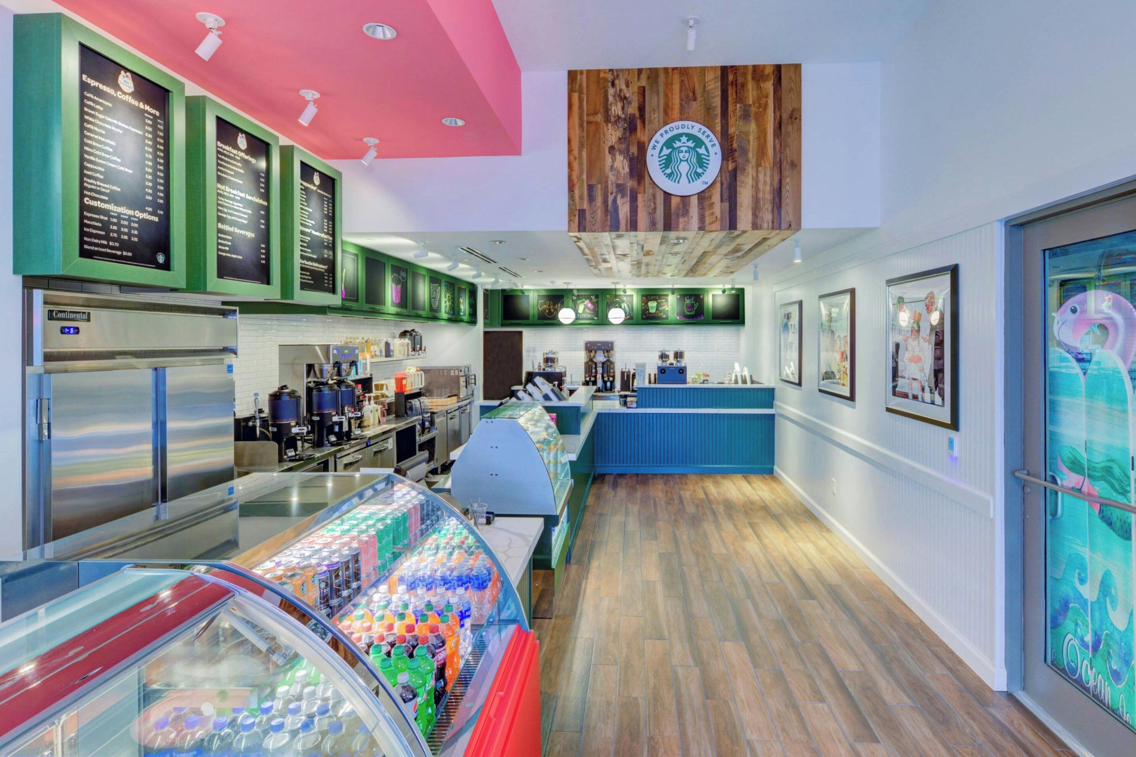 A modern coffee shop interior with a wooden ceiling, a Starbucks logo, a refrigerated display case, and a counter with a blue backdrop.