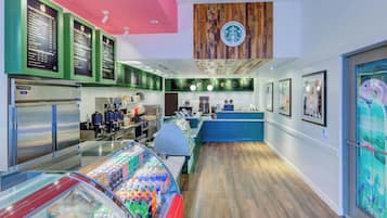 A modern coffee shop interior with a wooden ceiling, a Starbucks logo, a refrigerated display case, and a counter with a blue backdrop.