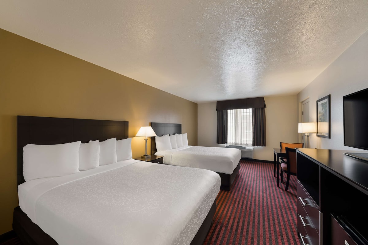 A hotel room with two beds, a desk, a TV, and a window with curtains.