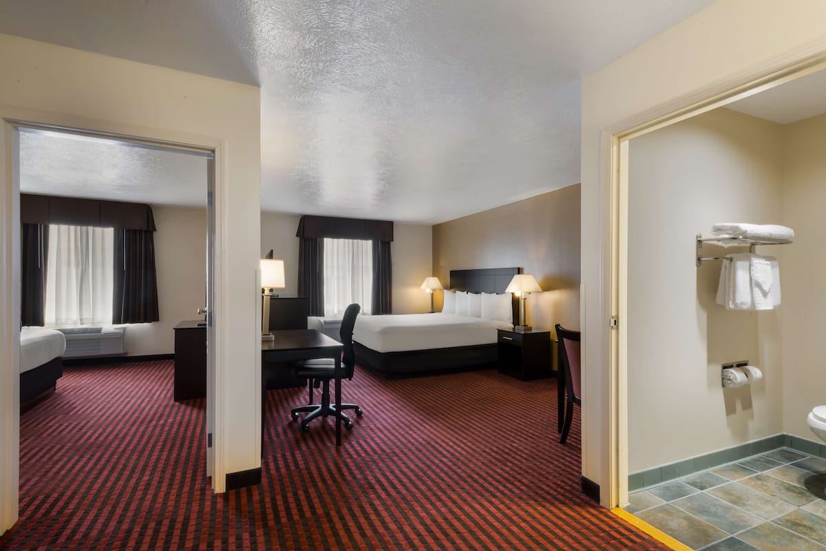 A hotel room with two beds, a desk, a chair, a bathroom, and a red patterned carpet.