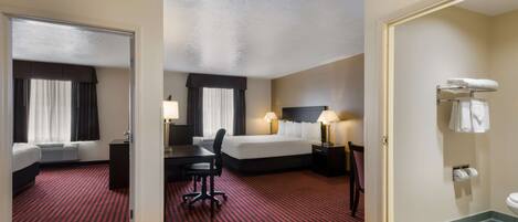 A hotel room with two beds, a desk, a chair, a bathroom, and a red patterned carpet.