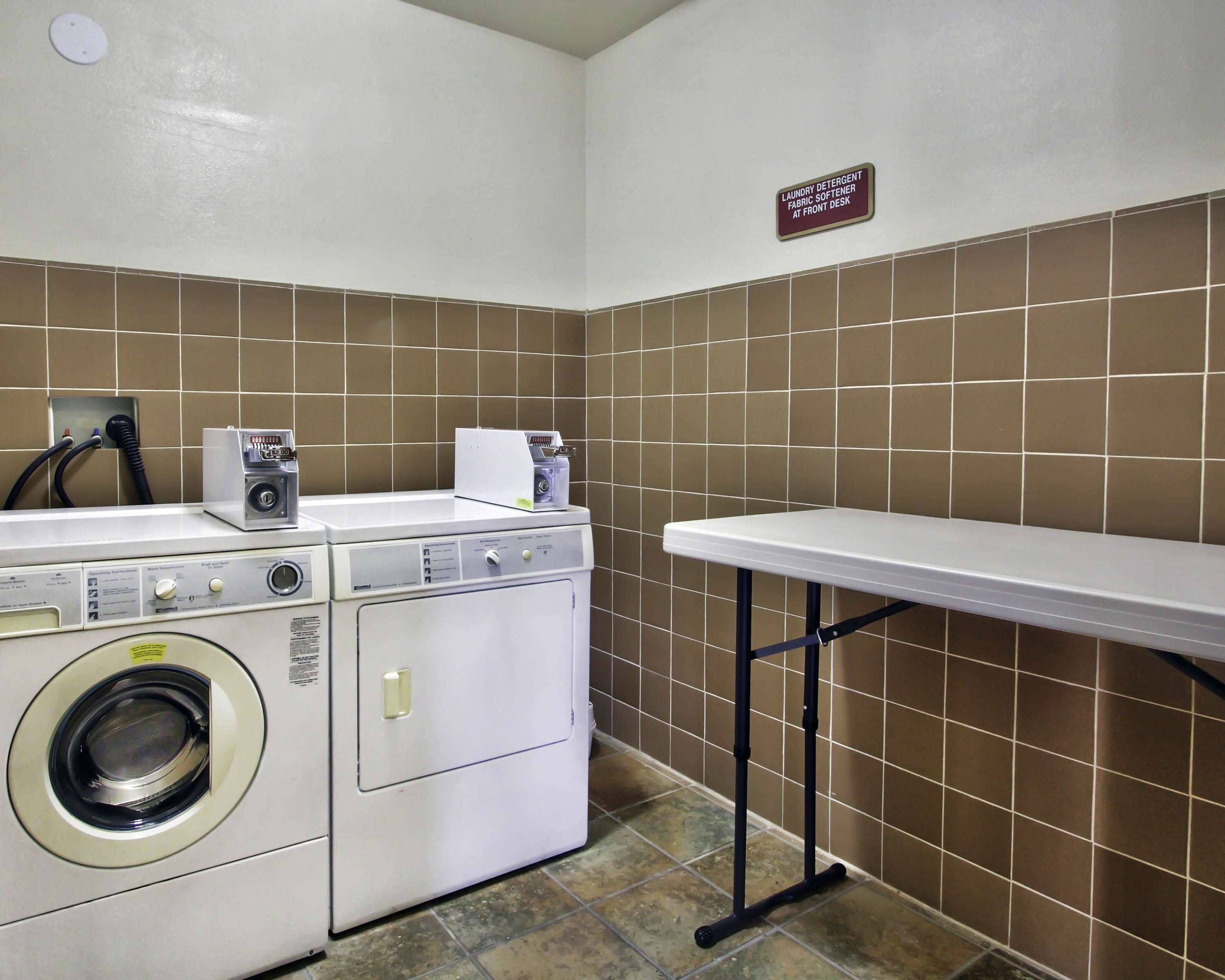 A laundry area with a washing machine, a dryer, and a sign indicating laundry detergent and fabric softener at the front desk.