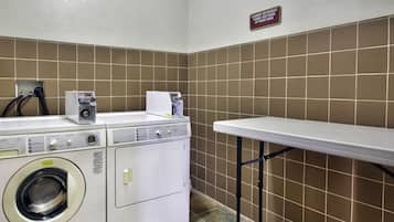 A laundry area with a washing machine, a dryer, and a sign indicating laundry detergent and fabric softener at the front desk.