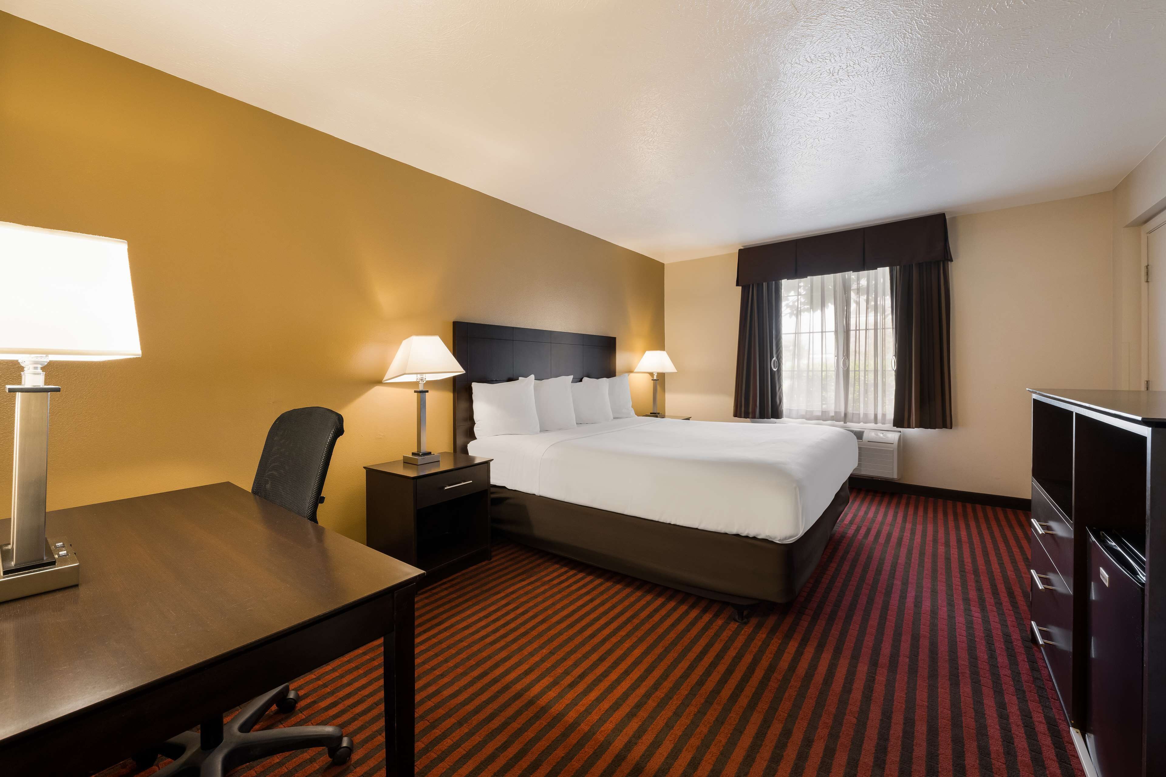 A hotel room with a large bed, two bedside tables with lamps, a desk, and a wardrobe.