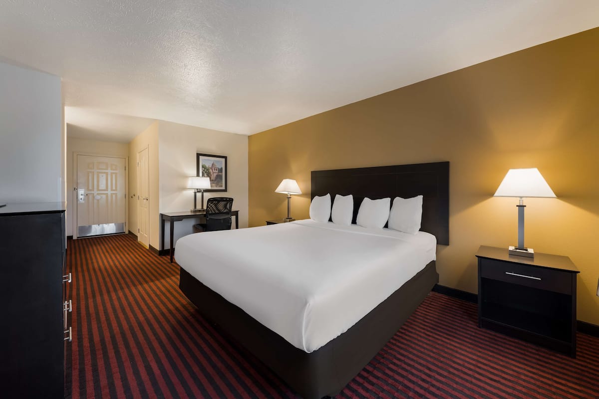 A hotel room with a large bed, two bedside tables with lamps, a desk, and a wardrobe.