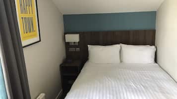 Et hotelværelse med en seng, et natbord, en lampe og et indramet skilt med 'HAPPY TOWN'.