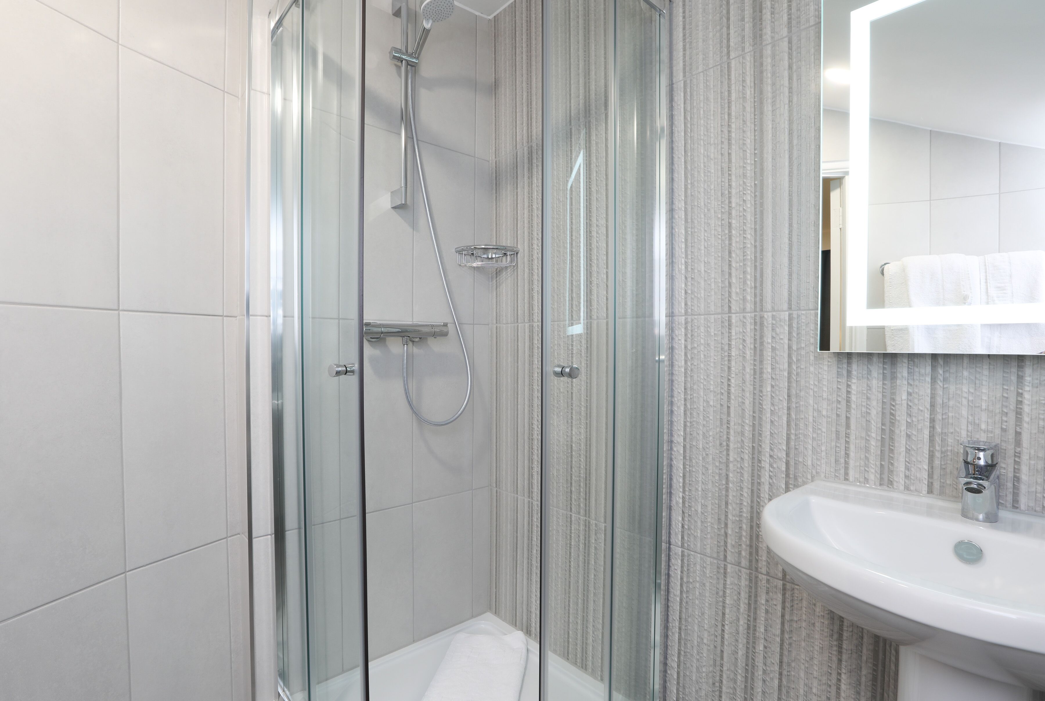 A modern bathroom with a glass-enclosed shower, a white sink, and a striped wall.