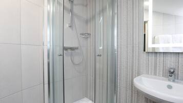 A modern bathroom with a glass-enclosed shower, a white sink, and a striped wall.