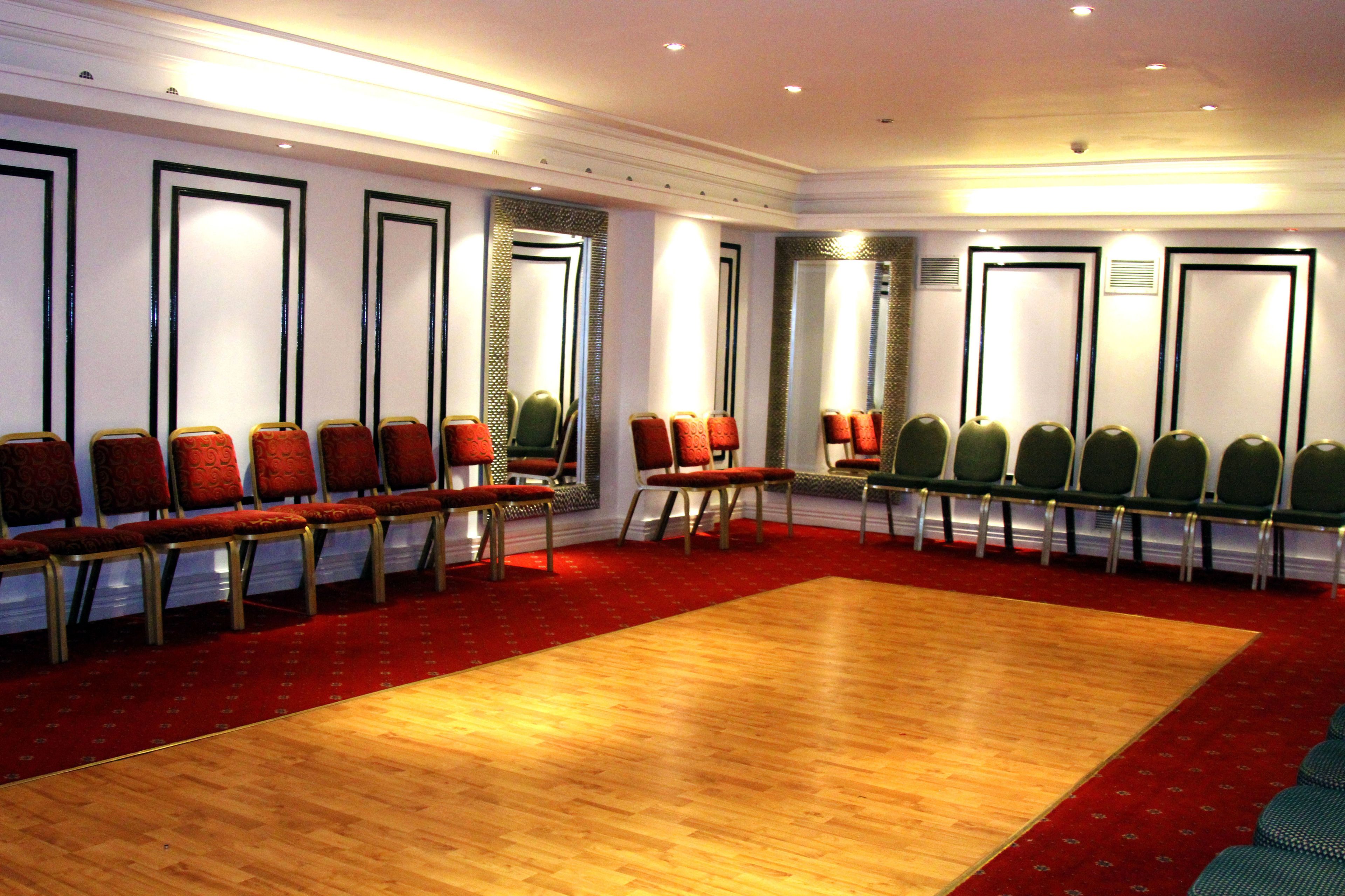 A conference room with rows of chairs, a large wooden floor, and a red carpet.