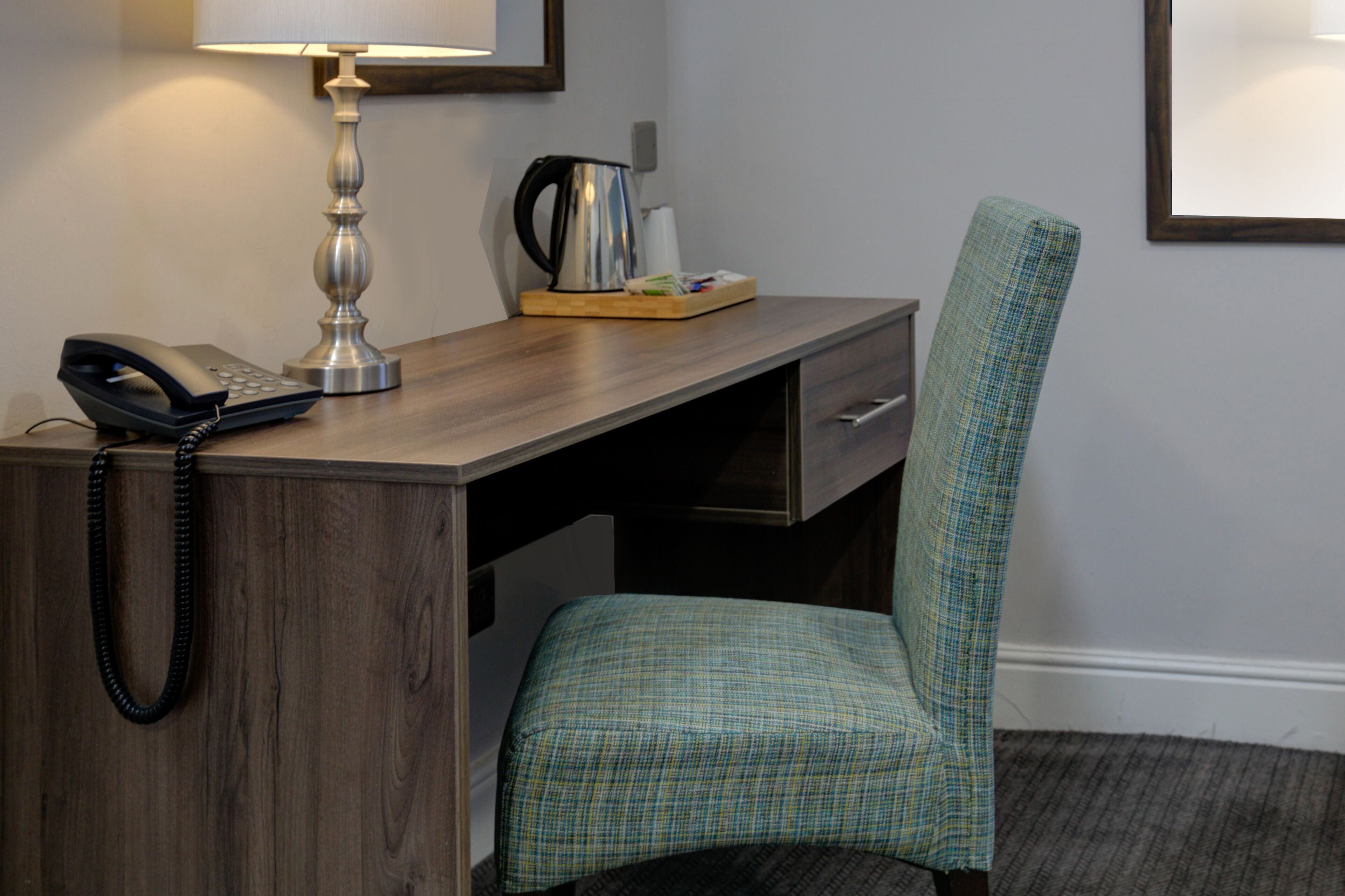 A hotel room with a wooden desk, a telephone, a lamp, a chair, and a coffee maker.