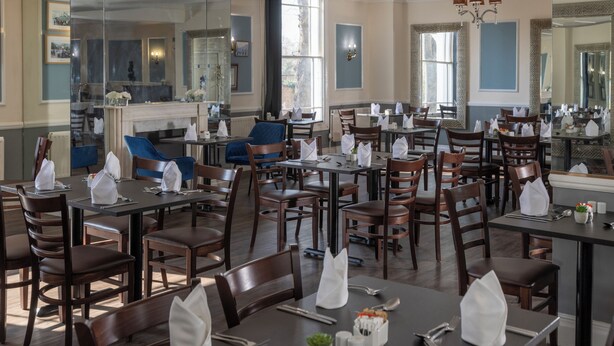 A dining area with multiple tables and chairs, a fireplace, and large windows. - The Jephson Hotel, BW Signature Collection (Royal Leamington Spa)