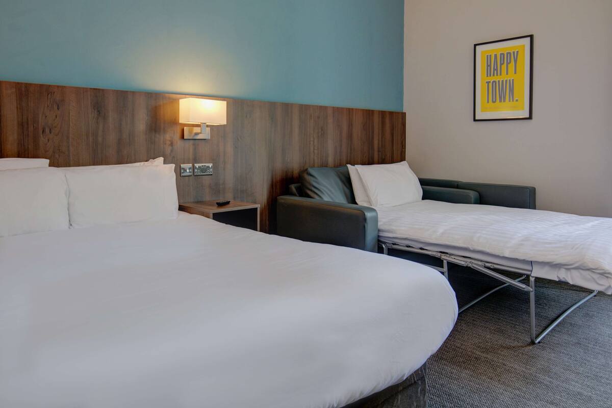 A hotel room with two beds, a nightstand with a lamp, and a framed sign on the wall.