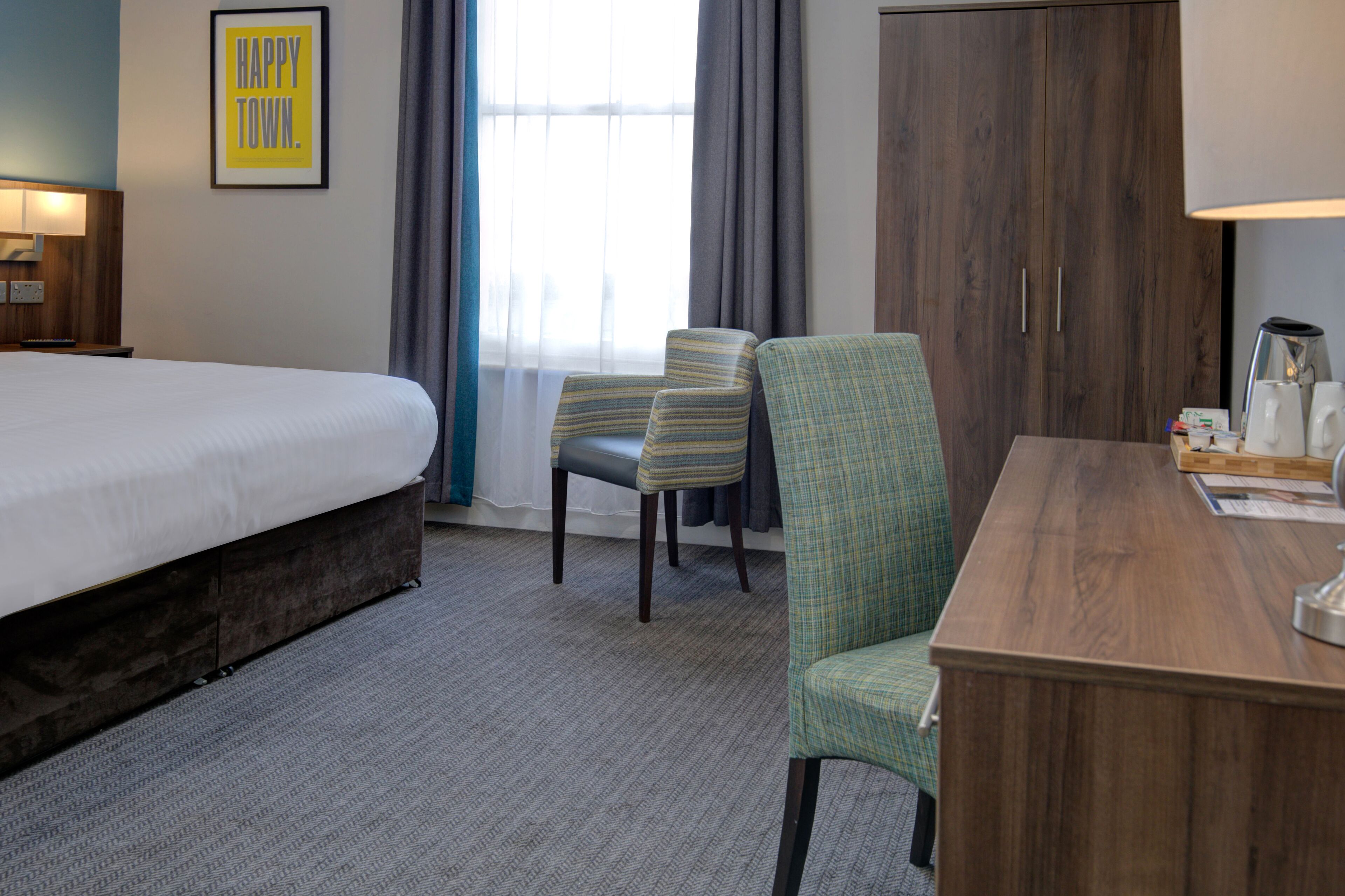 Une chambre d’hôtel avec un grand lit, deux chaises, un bureau, une lampe et une armoire.