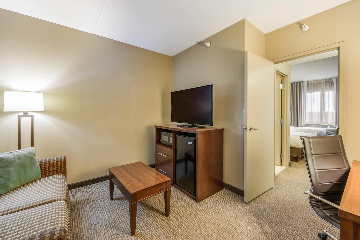 Une chambre d’hôtel avec un canapé, une petite table en bois, un téléviseur posé sur un meuble, un bureau et une chaise.