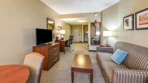 A hotel room with a TV, a wooden desk, a chair, a sofa, and a small table. - Comfort Suites Chicago O'Hare Airport (Schiller Park)