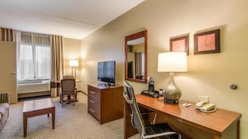 A hotel room with a desk, chair, television, lamp, and a bed with curtains.