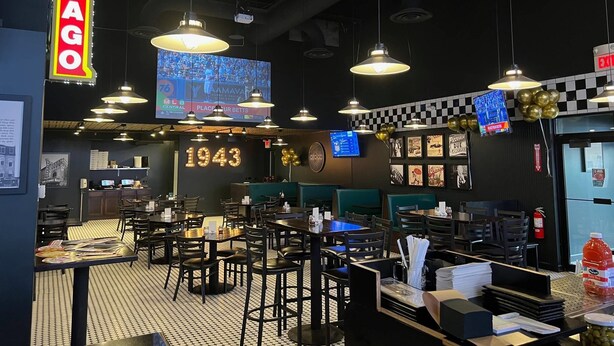 A restaurant interior with a retro 1943 theme, featuring hanging pendant lights, a checkered floor, and a large illuminated 'CHICAGO' sign. - Comfort Suites Chicago O'Hare Airport (Schiller Park)