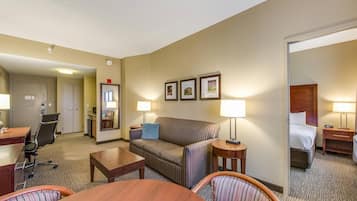 A hotel room with a sofa, two side tables with lamps, a desk with a chair, and a bed.
