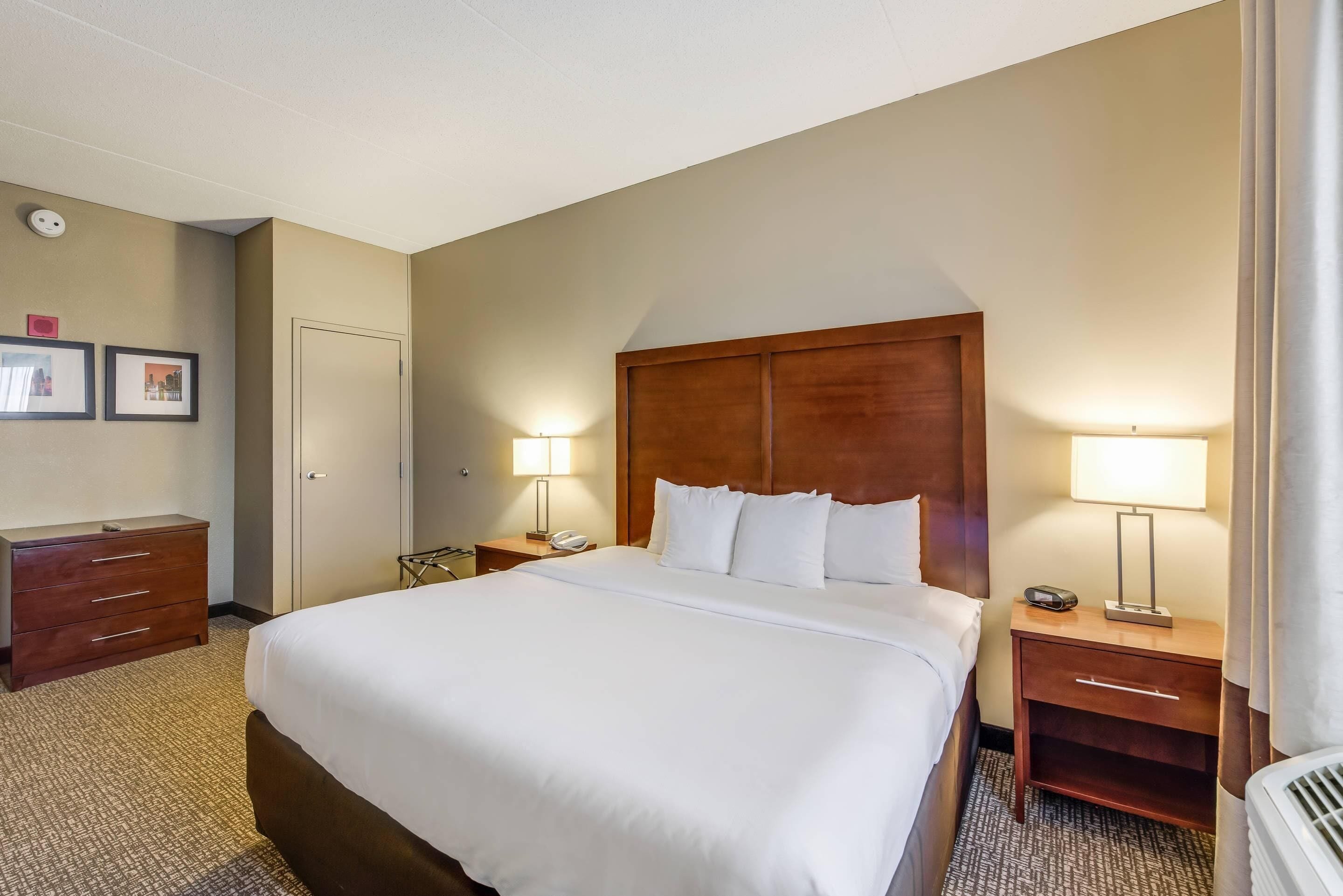 A hotel room with a large bed, two bedside tables with lamps, a wooden headboard, a wardrobe, and a door.
