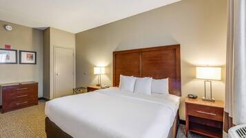 A hotel room with a large bed, two bedside tables with lamps, a wooden headboard, a wardrobe, and a door.