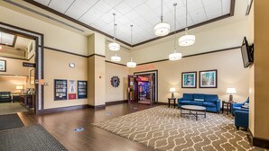 A hotel lobby with a patterned carpet, a blue sofa, a reception desk, and a sign for the restaurant. - Comfort Suites Chicago O'Hare Airport (Schiller Park)