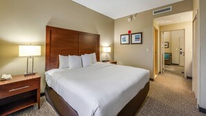 A hotel room with a large bed, two bedside tables with lamps, a wooden headboard, and a carpeted floor. - Comfort Suites Chicago O'Hare Airport (Schiller Park)