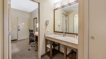 A hotel bathroom with a sink, mirror, hairdryer, and chair.